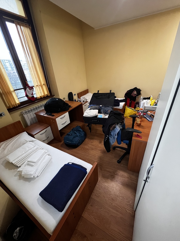 Weitwinkelbild vom Zimmer bei Ankunft. Man sieht zwei Betten, Tische und mein Gepäck